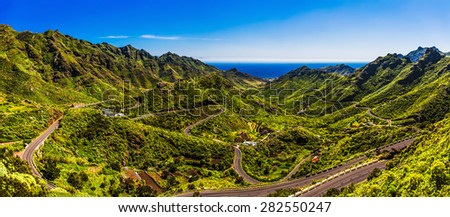 Green mountains or rocks with winding or serpantine road and blue sky with cloud and ocean on horizon landscape panorama in Tenerife Canary island, Spain at summer or spring