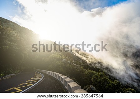 Asphalt road in mountains or rocks and sky with sun and sunlight and clouds over peak in Tenerife Canary island, Spain at sunset