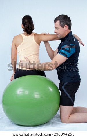 Man at the gym doing excercices to a woman with a swiss ball