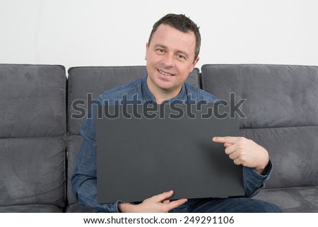 Smiling man sitting on sofa holding a blank black sign