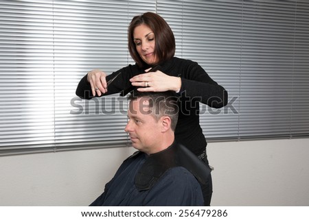 Barber cutting hair with scissors and comb, using cosmetic in spray, client is a  caucasian man