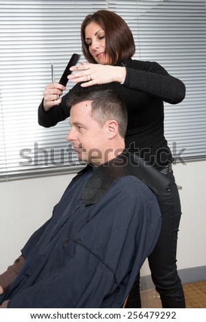 Barber cutting hair with scissors and comb, using cosmetic in spray, client is a  caucasian man