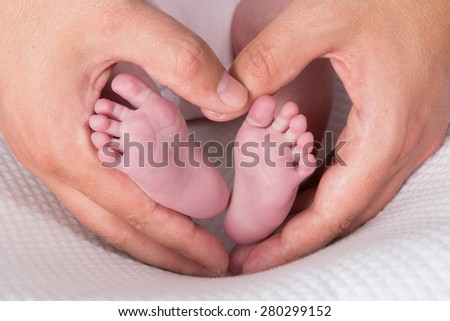Newborn baby feet on male hands, shape like a lovely heart
