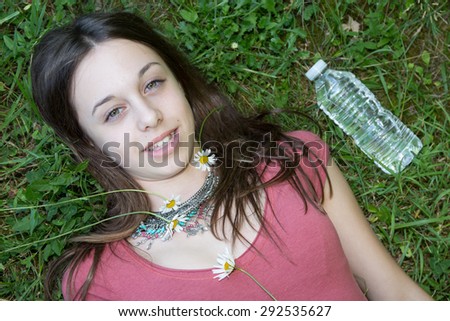Relaxed young person (teenage girl) lying in grass and flowers with stretched hand - closed eyes