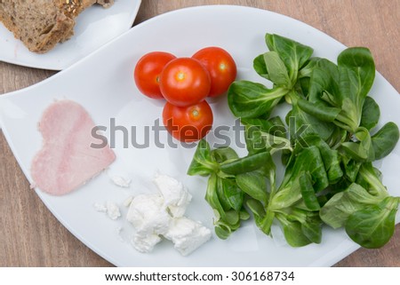 Tomato salad and heart shaped ham on wooden table