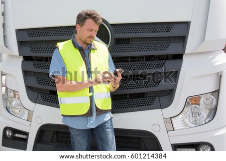 international truck driver in front of his truck with his mobile phone and his yellow safety vest