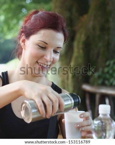 Young woman pouring tea from vacuum flask in a picnic in a park