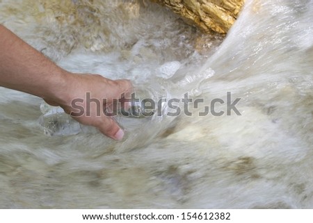 A man\'s hand filling up a bottle with fresh mountain spring water