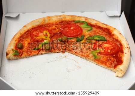 Half eaten pizza with tomatoes, cheese and sweet (bell) pepper in a paper take away box