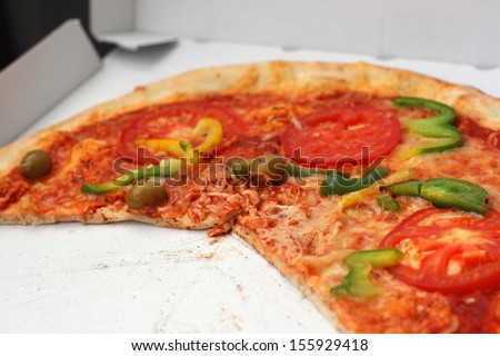 Half eaten pizza with tomatoes, cheese and sweet (bell) pepper in a paper take away box