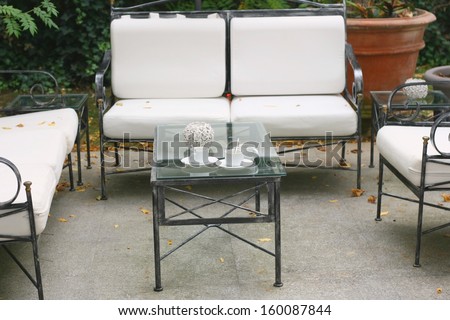 Sofa with white pillows and table with empty cups in a garden in autumn