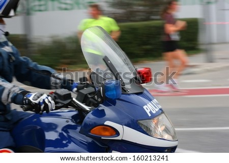 Front of a blue police motorcycle driving on a city street, focus on turn signal (indicator)