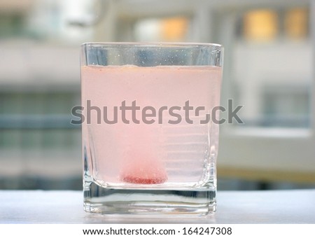 Coloured multi vitamin carbon tablet or effervescent pill making bubbles in a glass of water, in the morning on a window sill