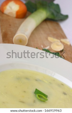 Hot leek soup in white plate with fresh leek on wooden background, healthy lunch