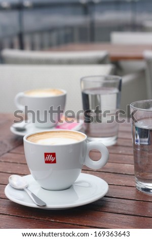 LJUBLJANA, SLOVENIA - JANUARY 01, 2014: Cup of illy espresso with milk, served with glass of water. Illycaffe is a worldwide coffee roasting company, its espresso is very popular in Slovenia and EU.