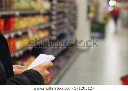 A man with shopping list, grocery store shelves and products in background