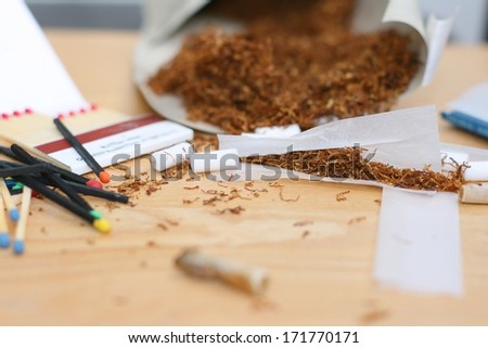 Rolling a cigarette, tobacco bag, rolling paper, filters and matches on a table, unhealthy life style. Focus on tobacco in rolling paper