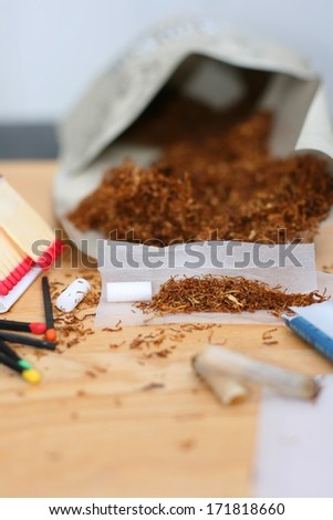 Rolling a cigarette, tobacco  (Nicotiana tabacum), rolling paper, filters and matches on a table, unhealthy life style. Focus on tobacco in the rolling paper