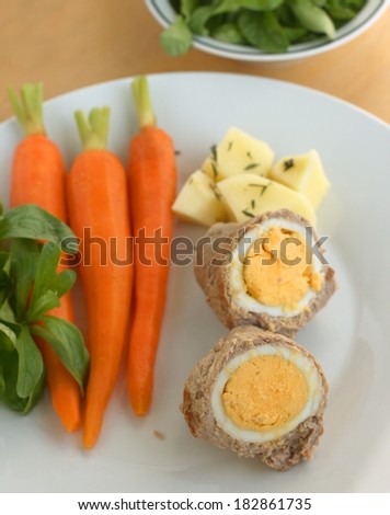 Easter lunch or dinner recipe idea, cooked egg in a roll of veal meat, served with cooked carrots, potato and fresh corn salad