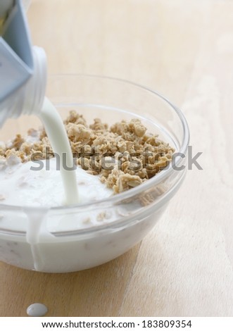 Preparing healthy breakfast, pouring low fat yogurt to crunchy muesli