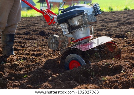 Farmer using modern mechanical rotary tiller with plow on a sunny day in a small farm