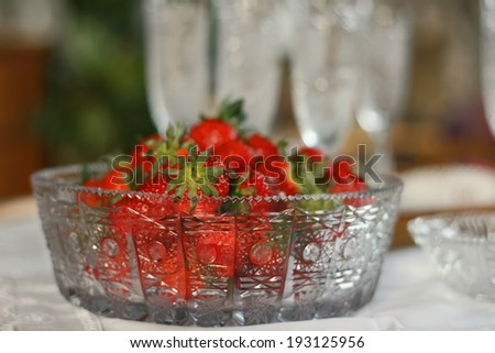 Expensive lead or crystal glass bowl with fresh delicious strawberries and crystal glass for champagne in background, shallow DOF, focus on bowl