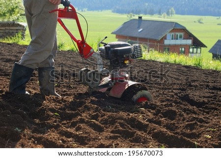 Farmer using modern mechanical rotary tiller with plow on a sunny day in a small farm