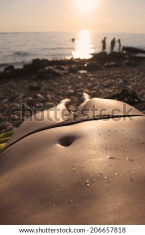 Woman lying on the beach looking at sunset with drops of water, focus on navel, point of view shot
