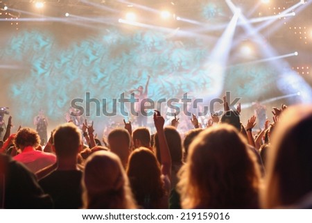 People attending pop concert, silhouettes of crowd dancing in front of stage, shallow DOF