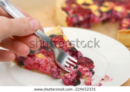 Eating a piece of delicious raspberry, blueberry and blackberry sweet pie on a plate, woman's hand holding a fork