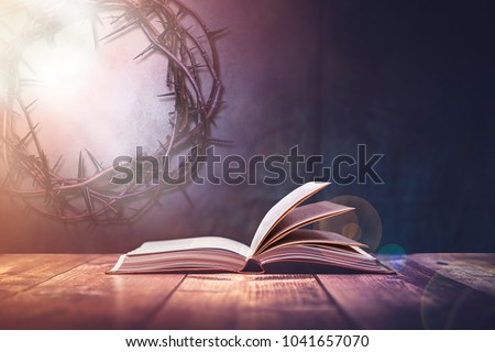 Open Bible with a light coming from above on a wooden desk and a Crown of Thorns in the wall.