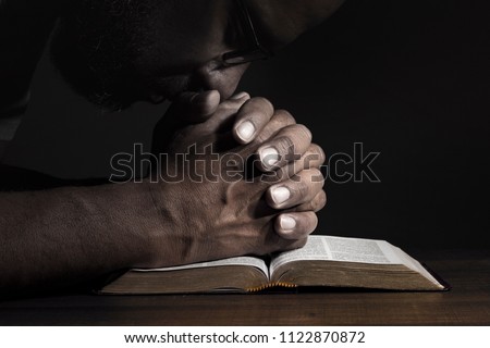 Man praying to God on a Bible in a dark place.