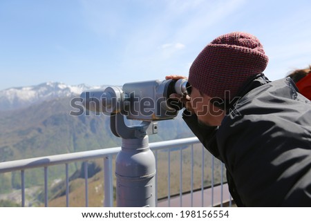 A man looking through coin operated high powered binoculars on a scenic mountain lookout.