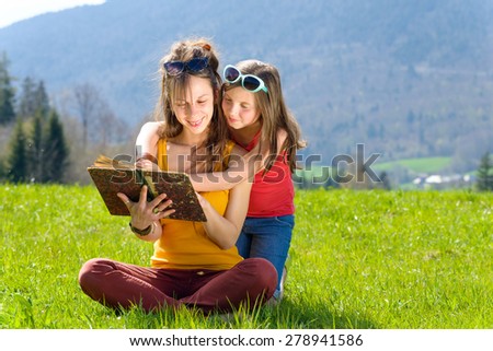 Mom and daughter reading a book in the meadow