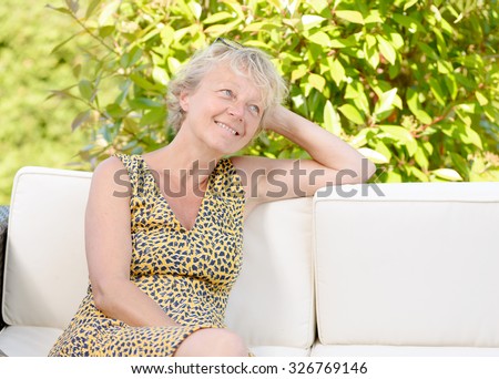 smiling blonde woman sitting on the sofa , in a garden