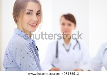Happy smiling female patient with two cheerful doctors in the background. Medical and health care concept