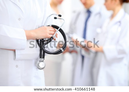 Female doctor holding a stethoscope in his hand, two doctors and patient are on the background