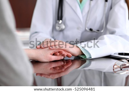 Friendly female doctor hands holding patient hand sitting at the desk for encouragement, empathy, cheering and support while medical examination. Bad news lessening, trust and ethics concept