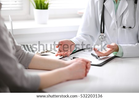 Close up of doctor and  patient  sitting at the desk near the window in hospital
