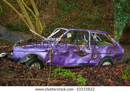 A dumped car in a pleasant woodland scene by a stream
