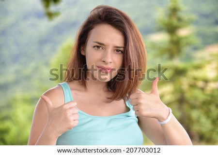 Beautiful young woman giving thumbs up sign in the mountains