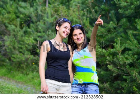 Two beautiful girls walking on a path in the forest. One pointing to the other.