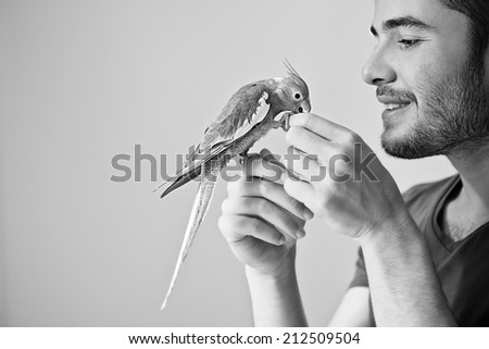 Attractive man playing with his parrot indoors. Black and white photograph