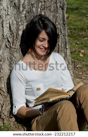 Beautiful young woman reading a book outside in park