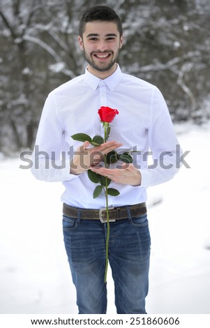 Portrait of a handsome man dressed in a white shirt and holding a rose, surrounded by snow.
