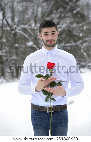 Portrait of a handsome man dressed in a white shirt and holding a rose, surrounded by snow.