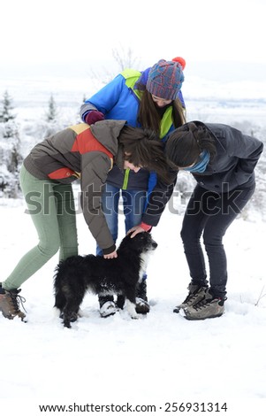 Three young women petting small black dog outside in winter.