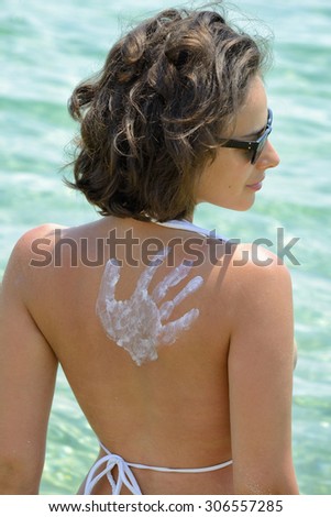 Woman in bikini looking at the ocean on hot summer day with cream hand on back