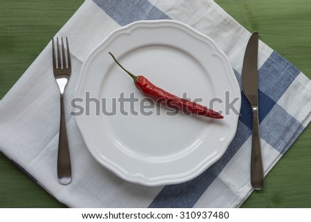 white plate with red chili and cutlery on towel and green wooden surface