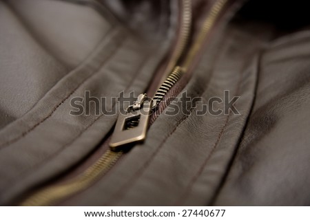A brown leather jacket close up shot. Focus is on zip.